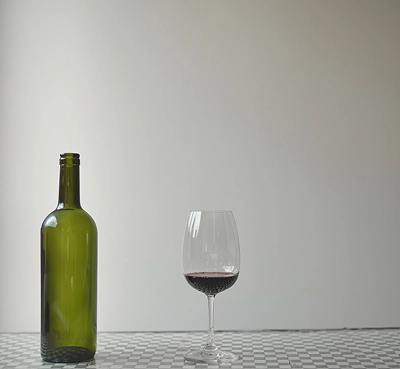 Зеленая бутылка вина и бокал с красным вином на шахматной поверхности